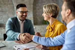 Happy financial advisor shaking hands with a couple after successful meeting in the office.