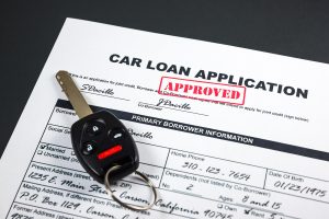 Filled-up car loan application form with approved stamp and a remote car key